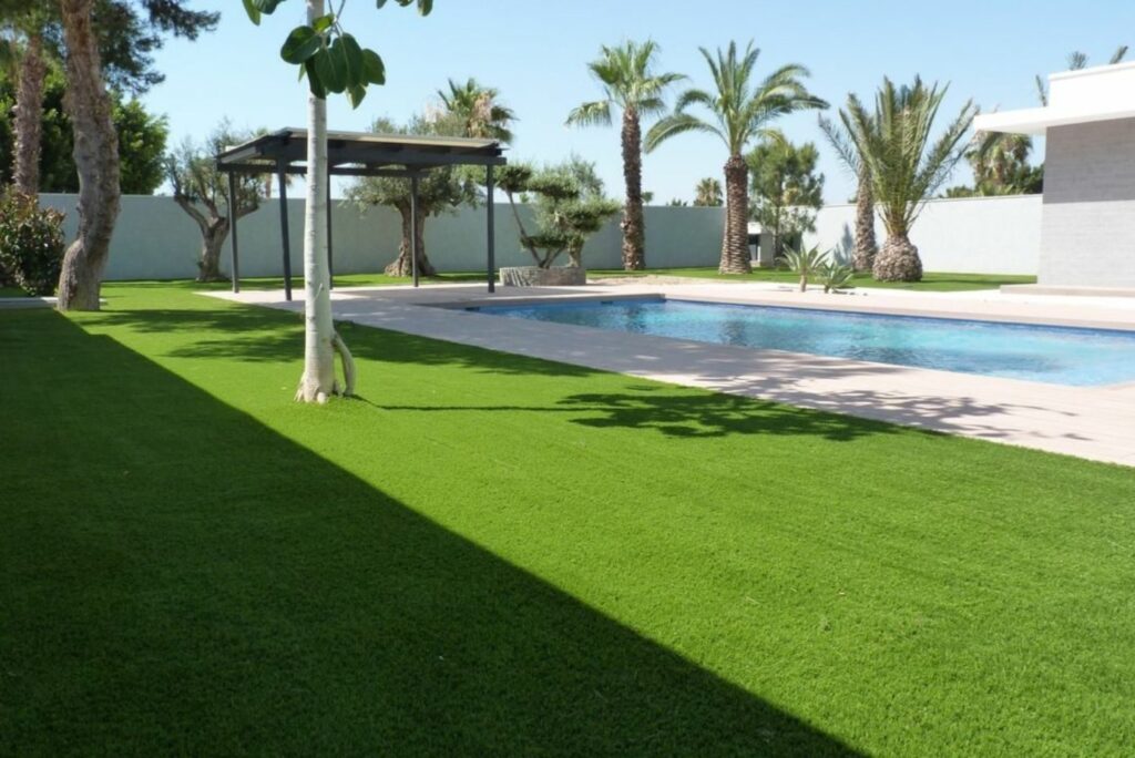 Jardín con césped artificial instalado por Flor & Design junto a una piscina en Gran Canaria